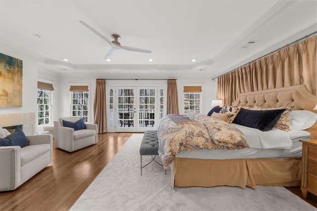 bedroom featuring wood finished floors, a fireplace, recessed lighting, a raised ceiling, and access to outside