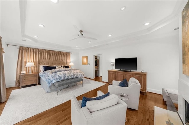 bedroom with a ceiling fan, a tray ceiling, wood finished floors, recessed lighting, and baseboards