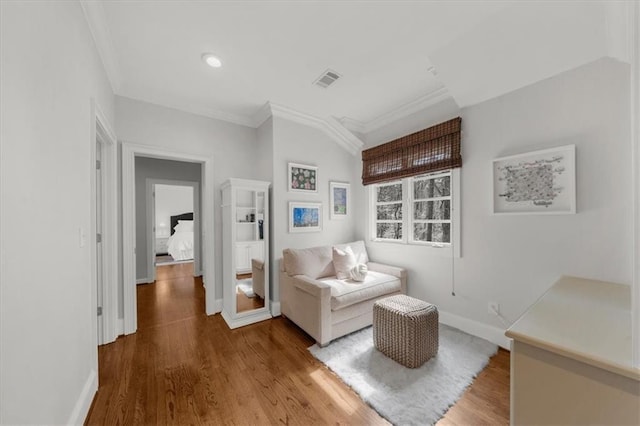 living area featuring visible vents, baseboards, wood finished floors, and crown molding