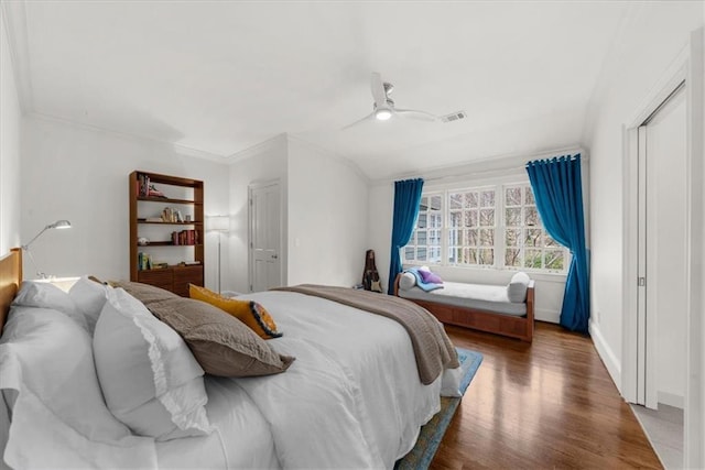 bedroom with a ceiling fan, wood finished floors, visible vents, baseboards, and crown molding