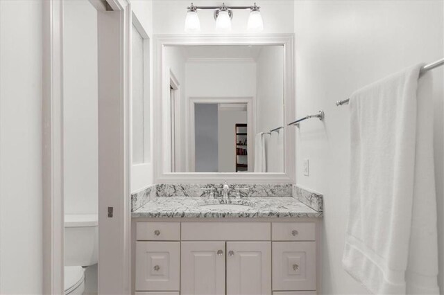 bathroom featuring toilet, ornamental molding, and vanity
