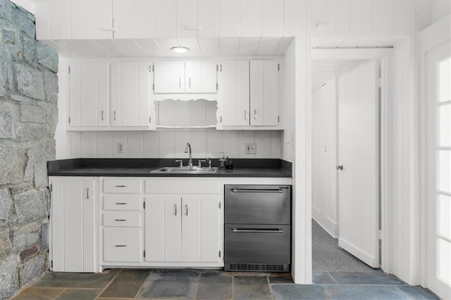 kitchen with dark countertops, white cabinets, stone finish floor, and a sink