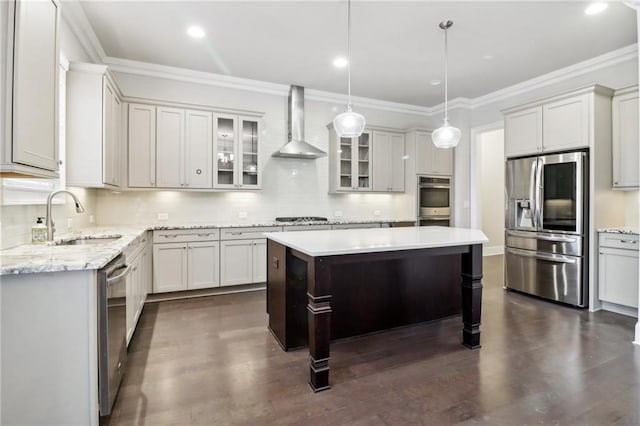 kitchen featuring sink, wall chimney range hood, decorative light fixtures, a kitchen island, and appliances with stainless steel finishes