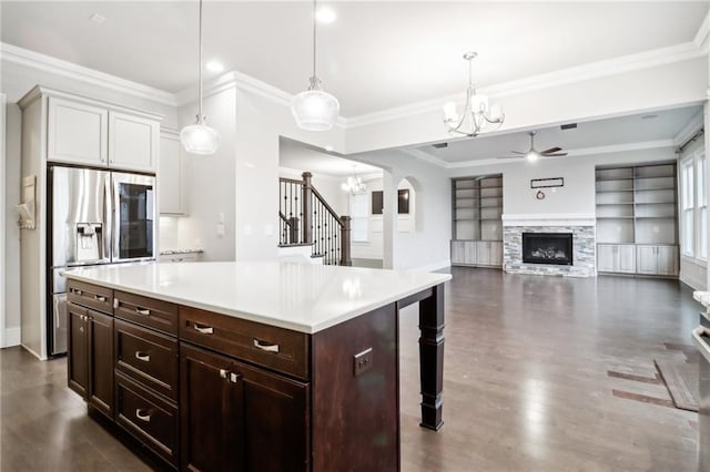 kitchen featuring stainless steel fridge, ceiling fan with notable chandelier, a center island, a stone fireplace, and hanging light fixtures