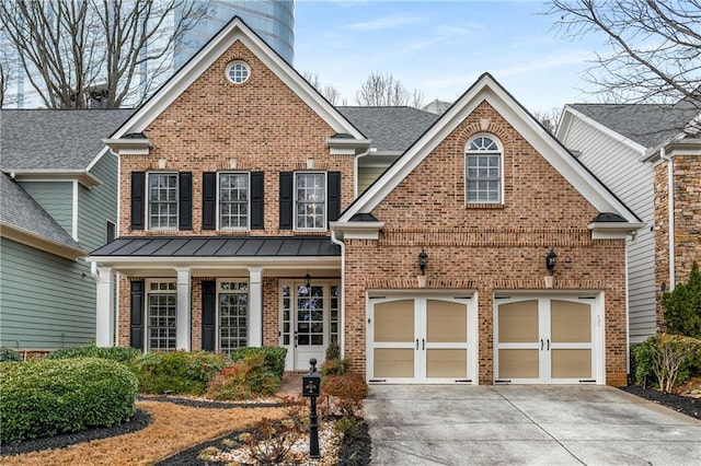 traditional-style home featuring brick siding, concrete driveway, roof with shingles, metal roof, and a standing seam roof