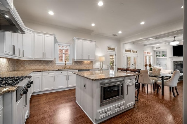 kitchen featuring dark wood-type flooring, under cabinet range hood, light stone counters, appliances with stainless steel finishes, and white cabinetry