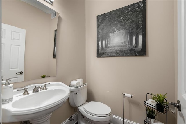 half bath with visible vents, toilet, baseboards, and a sink