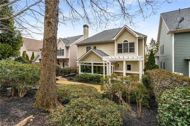 back of property with a shingled roof, a chimney, and a pergola