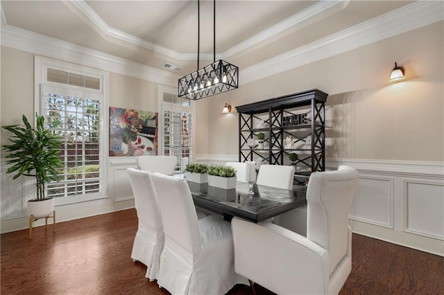 dining area featuring a tray ceiling, a wainscoted wall, visible vents, and dark wood finished floors