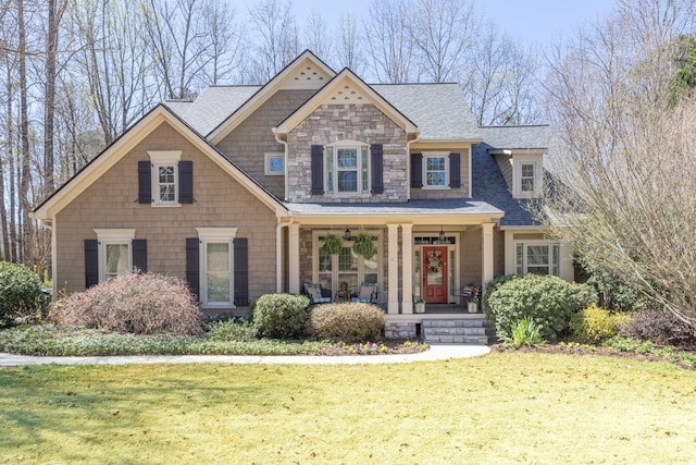 view of front of home with a porch, a front lawn, stone siding, and roof with shingles