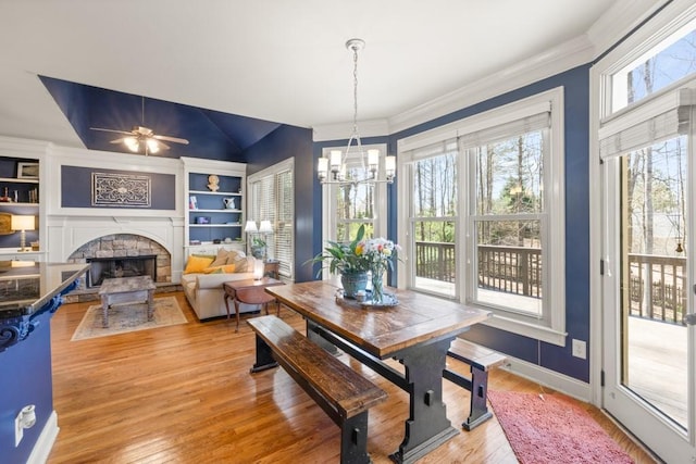 dining area with built in features, baseboards, a stone fireplace, light wood-style floors, and crown molding