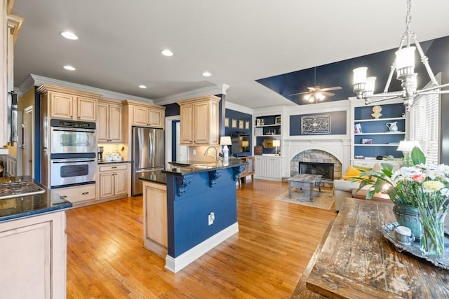 kitchen featuring ceiling fan with notable chandelier, light wood-style flooring, light brown cabinetry, appliances with stainless steel finishes, and open floor plan
