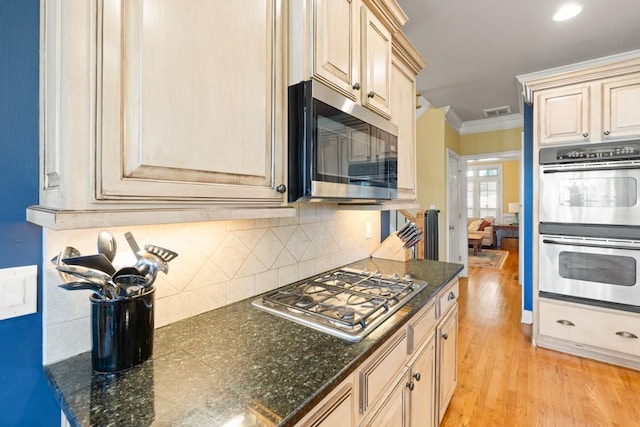 kitchen featuring visible vents, appliances with stainless steel finishes, light wood-type flooring, crown molding, and backsplash