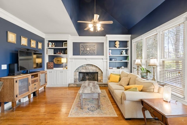 living area with a stone fireplace, vaulted ceiling, a ceiling fan, built in shelves, and wood finished floors