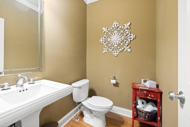half bath featuring baseboards, a sink, toilet, and wood finished floors