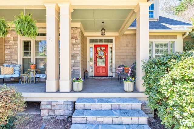 doorway to property with stone siding, a shingled roof, and covered porch