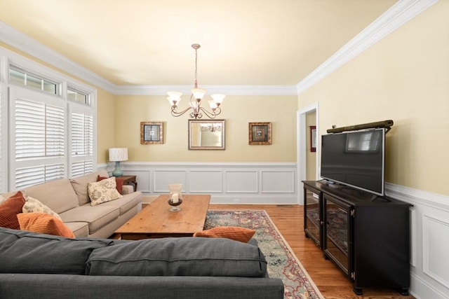 living area featuring an inviting chandelier, wainscoting, light wood-type flooring, and crown molding