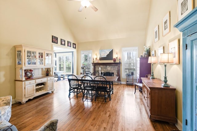 dining area featuring baseboards, a stone fireplace, ceiling fan, wood finished floors, and high vaulted ceiling
