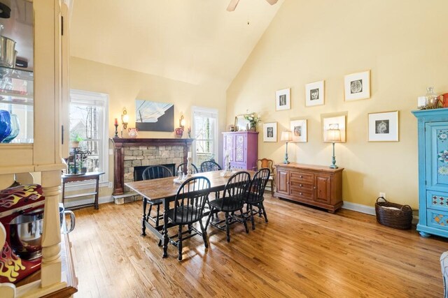 dining space with baseboards, a ceiling fan, light wood-type flooring, a fireplace, and high vaulted ceiling