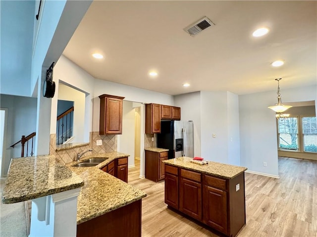 kitchen with visible vents, light wood finished floors, a sink, decorative backsplash, and stainless steel fridge