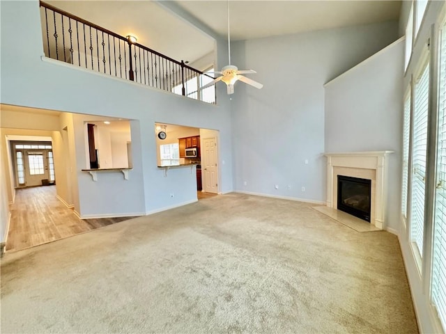 unfurnished living room with baseboards, a high ceiling, a fireplace, ceiling fan, and carpet flooring