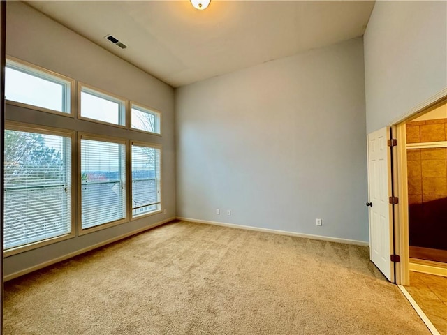 unfurnished room with visible vents, light carpet, baseboards, and a towering ceiling