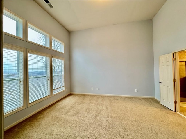 spare room with visible vents, baseboards, light colored carpet, and a high ceiling