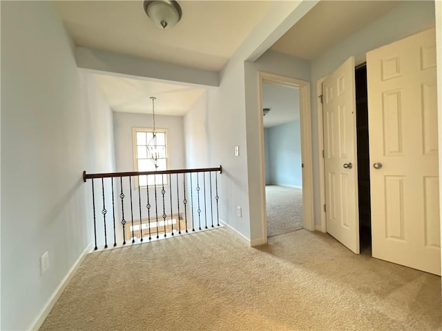 hallway featuring baseboards, an inviting chandelier, and carpet flooring