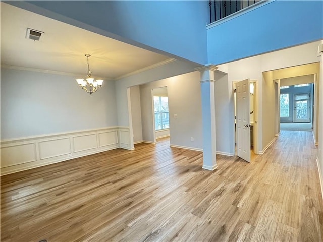 empty room featuring visible vents, a notable chandelier, light wood-style flooring, crown molding, and ornate columns