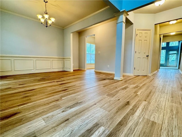 spare room with wood finished floors, a wainscoted wall, ornate columns, crown molding, and a notable chandelier