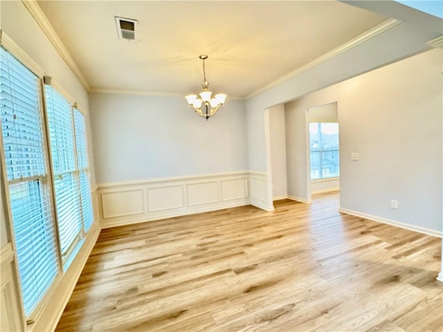 empty room featuring visible vents, a notable chandelier, ornamental molding, wainscoting, and light wood finished floors