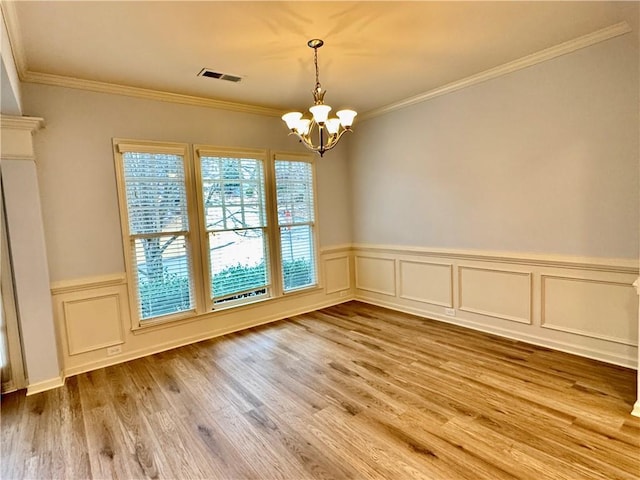 spare room with crown molding, wood finished floors, visible vents, and a chandelier