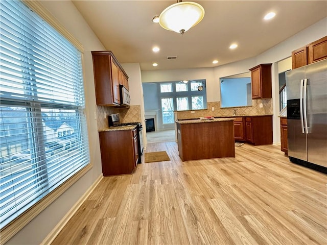 kitchen featuring backsplash, a kitchen island, light wood-type flooring, a glass covered fireplace, and stainless steel appliances