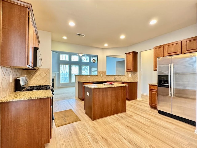 kitchen featuring visible vents, backsplash, light wood-type flooring, brown cabinetry, and stainless steel appliances