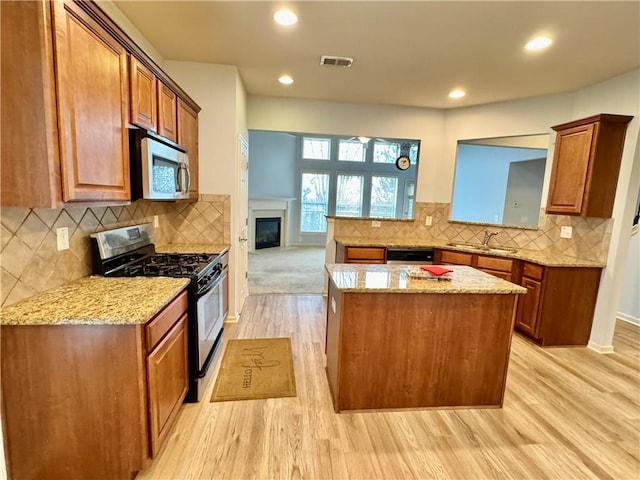 kitchen with a center island, brown cabinets, light wood finished floors, and stainless steel appliances