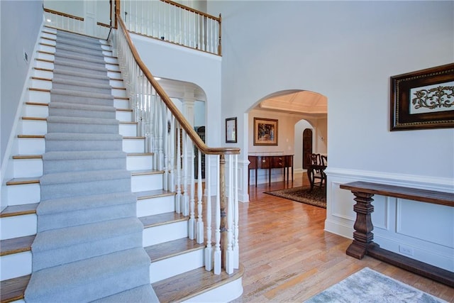 foyer entrance featuring arched walkways, a wainscoted wall, wood finished floors, stairs, and a high ceiling