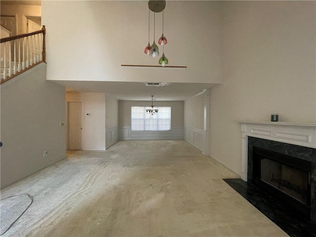 unfurnished living room with carpet floors, a high end fireplace, a high ceiling, and a notable chandelier