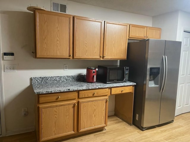 kitchen featuring stainless steel fridge, built in desk, light stone counters, and light hardwood / wood-style floors