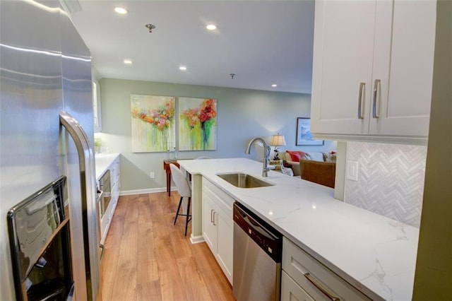 kitchen with light stone countertops, appliances with stainless steel finishes, white cabinets, sink, and backsplash