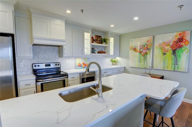 kitchen featuring light stone countertops, white cabinetry, appliances with stainless steel finishes, and custom range hood