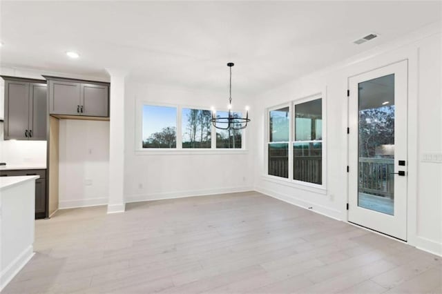 unfurnished dining area with a chandelier, plenty of natural light, light wood-style flooring, and visible vents