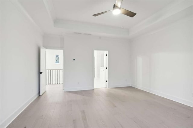 spare room featuring a tray ceiling, wood finished floors, baseboards, and a ceiling fan