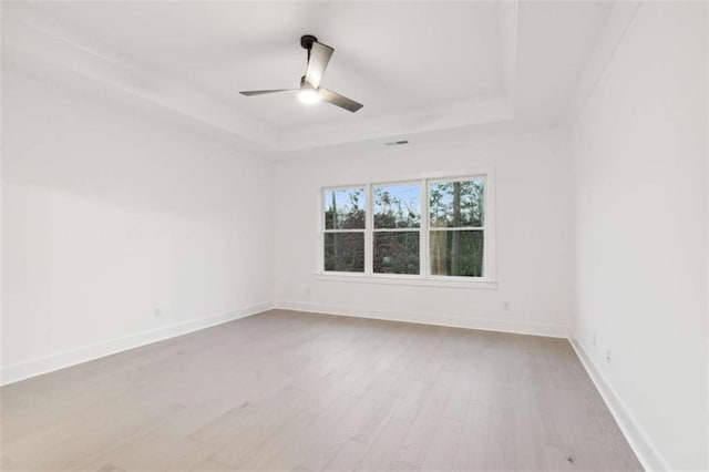 empty room with a tray ceiling, baseboards, a ceiling fan, and wood finished floors