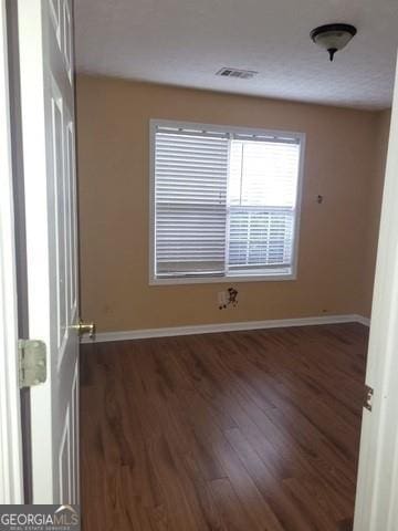 unfurnished room featuring dark wood-style flooring, visible vents, and baseboards