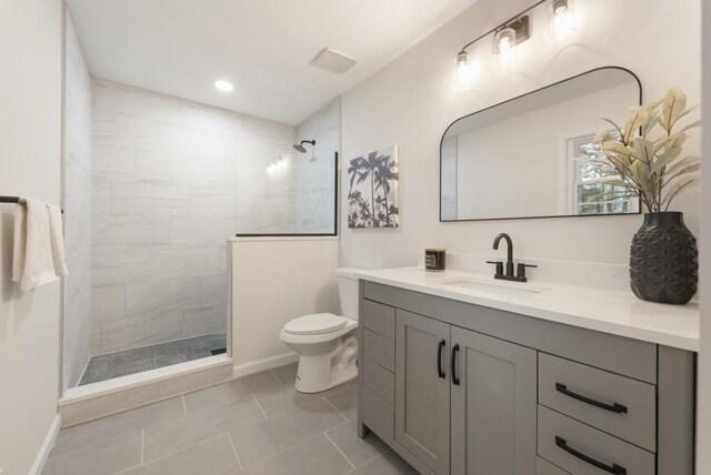 bathroom with tile patterned flooring, vanity, toilet, and tiled shower