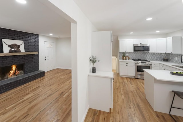 kitchen with sink, stainless steel appliances, decorative backsplash, white cabinets, and light wood-type flooring