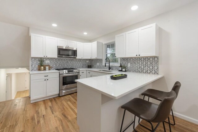 kitchen with kitchen peninsula, a breakfast bar, stainless steel appliances, sink, and white cabinetry