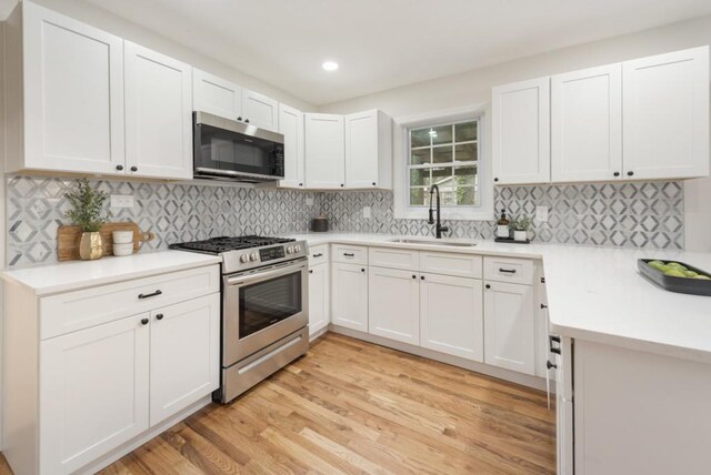 kitchen with white cabinets, sink, light hardwood / wood-style flooring, decorative backsplash, and stainless steel appliances