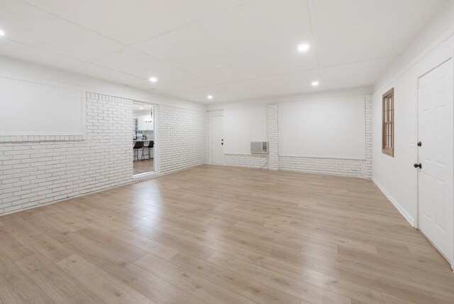 basement with a wall unit AC, light hardwood / wood-style flooring, and brick wall