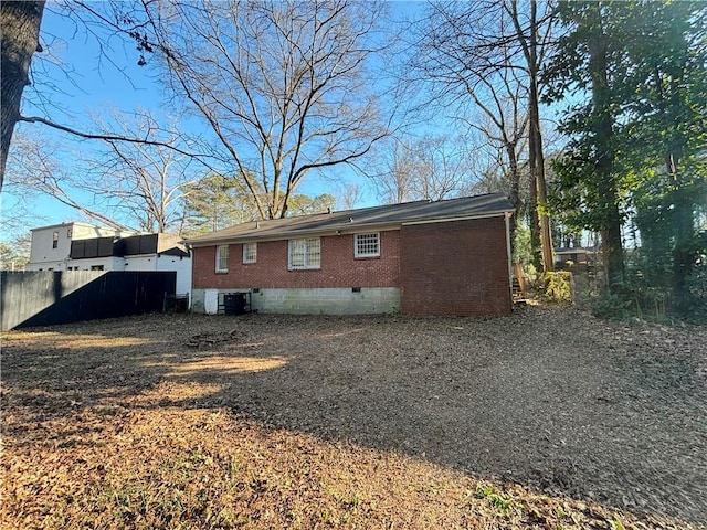 back of property with central AC unit, crawl space, fence, and brick siding